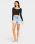Woman wearing a black long-sleeve top and light blue denim shorts on a white background