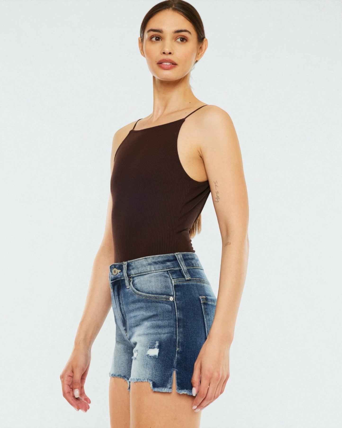 Woman wearing a brown bodysuit and denim shorts on a white background