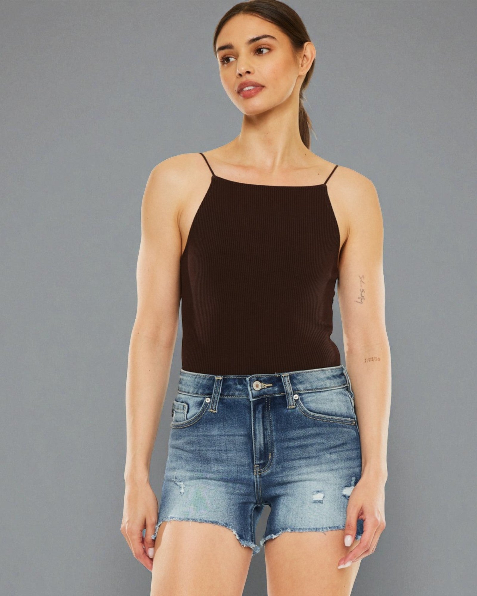 Woman wearing a black tank top and denim shorts against a gray background