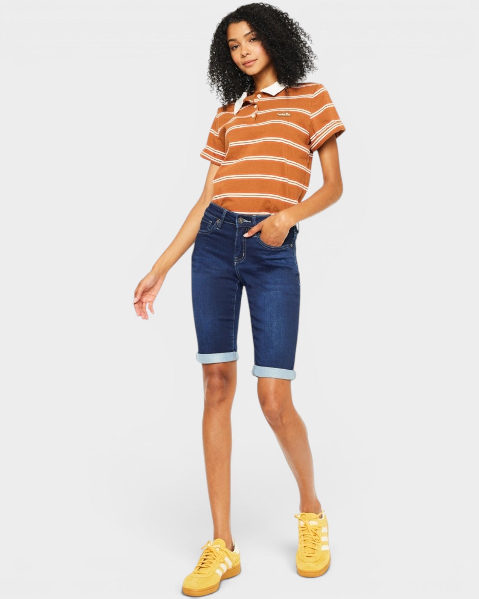 Woman wearing a striped shirt, blue denim shorts, and yellow sneakers on a white background