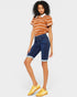 Woman wearing a striped polo shirt and blue denim shorts on a plain background