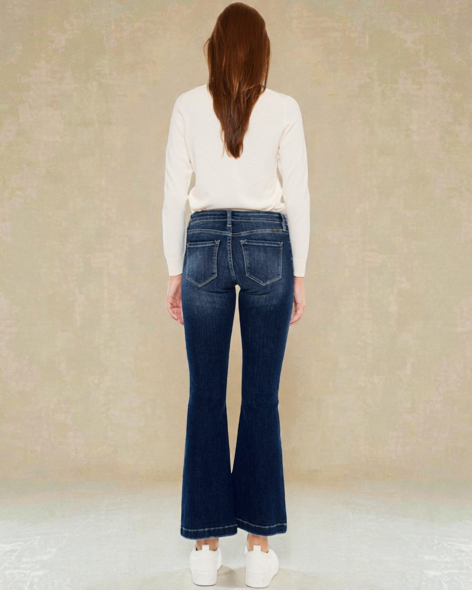 Woman wearing blue jeans and a white sweater against a beige background