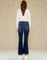 Woman wearing blue jeans and a white sweater against a beige background
