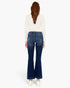 A woman viewed from the back wearing dark blue flared jeans, a cream long-sleeve top, and white sneakers against a plain white studio background.
