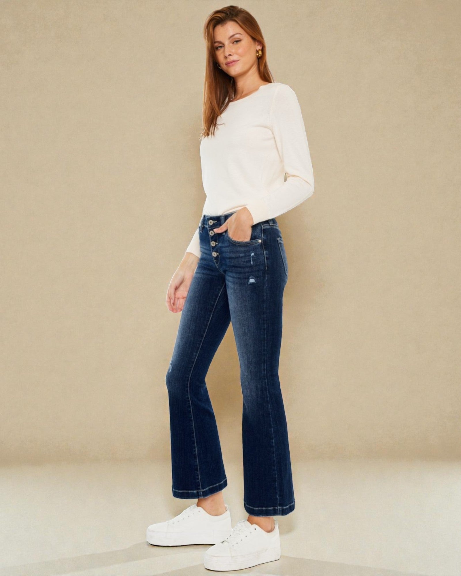 Woman wearing blue jeans and a white top against a beige background
