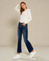 Woman wearing a white sweater and blue jeans against a beige background