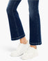A close-up of a person's legs wearing dark blue flared denim jeans and white platform sneakers against a clean white background.
