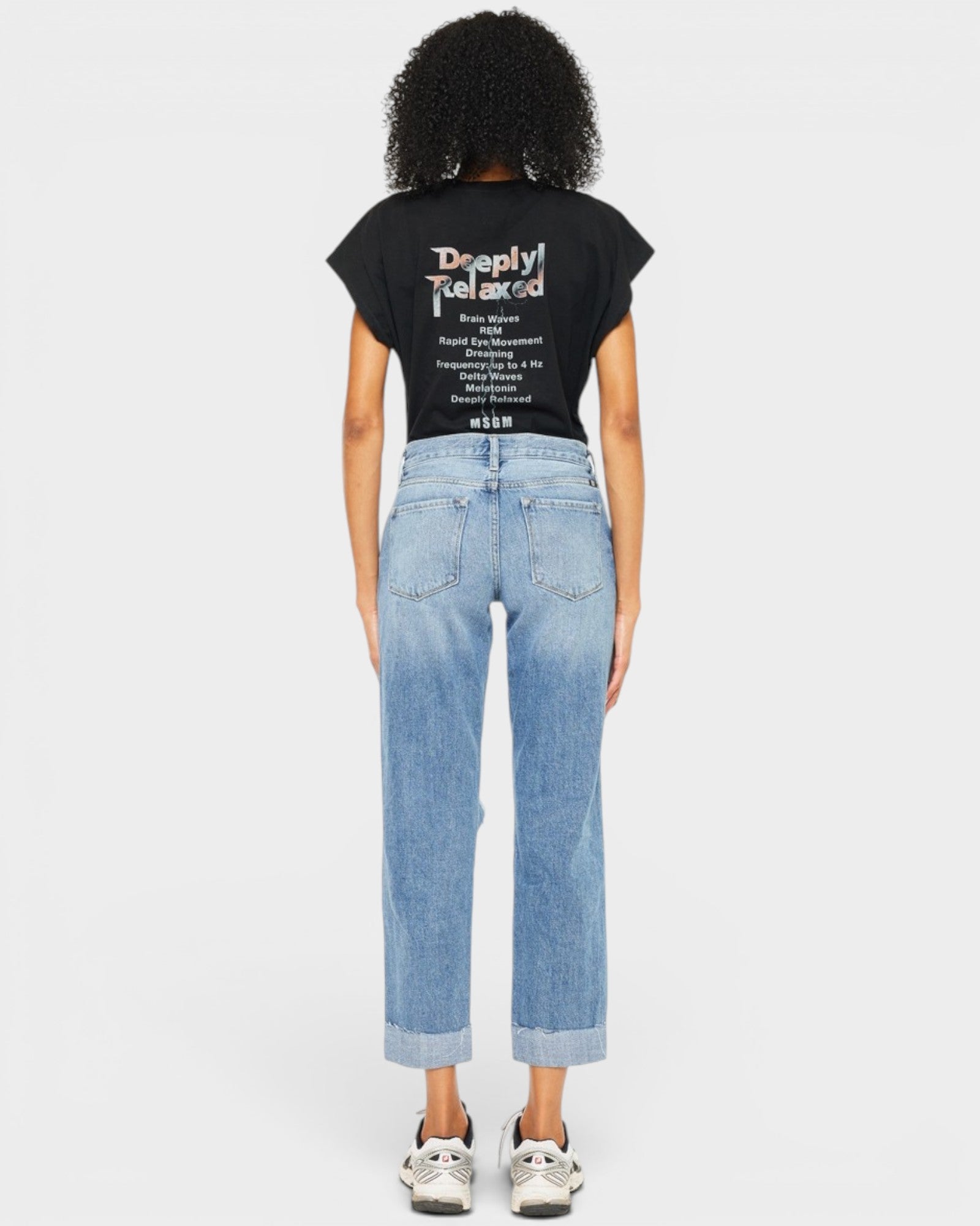 Person wearing a black t-shirt with text and light blue jeans on a white background