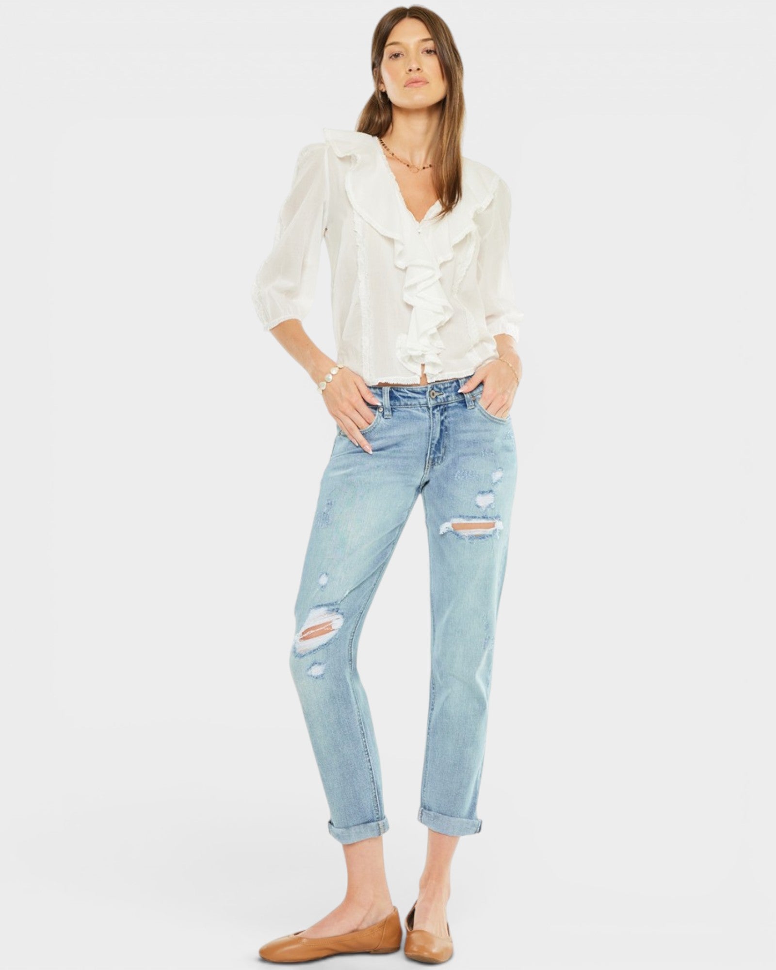 Woman wearing a white blouse and light blue ripped jeans on a white background