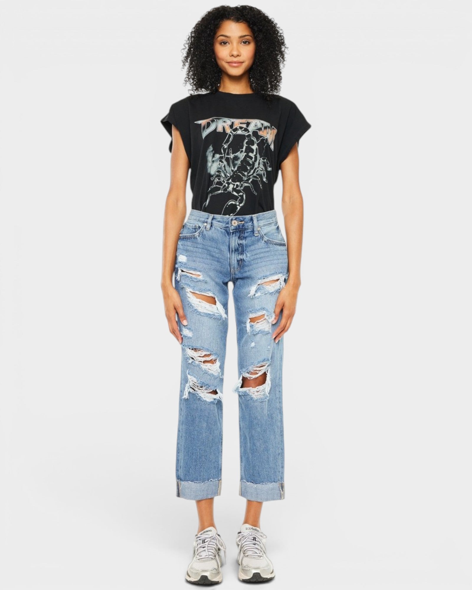 Person wearing a black t-shirt with graphic design and ripped blue jeans on a white background