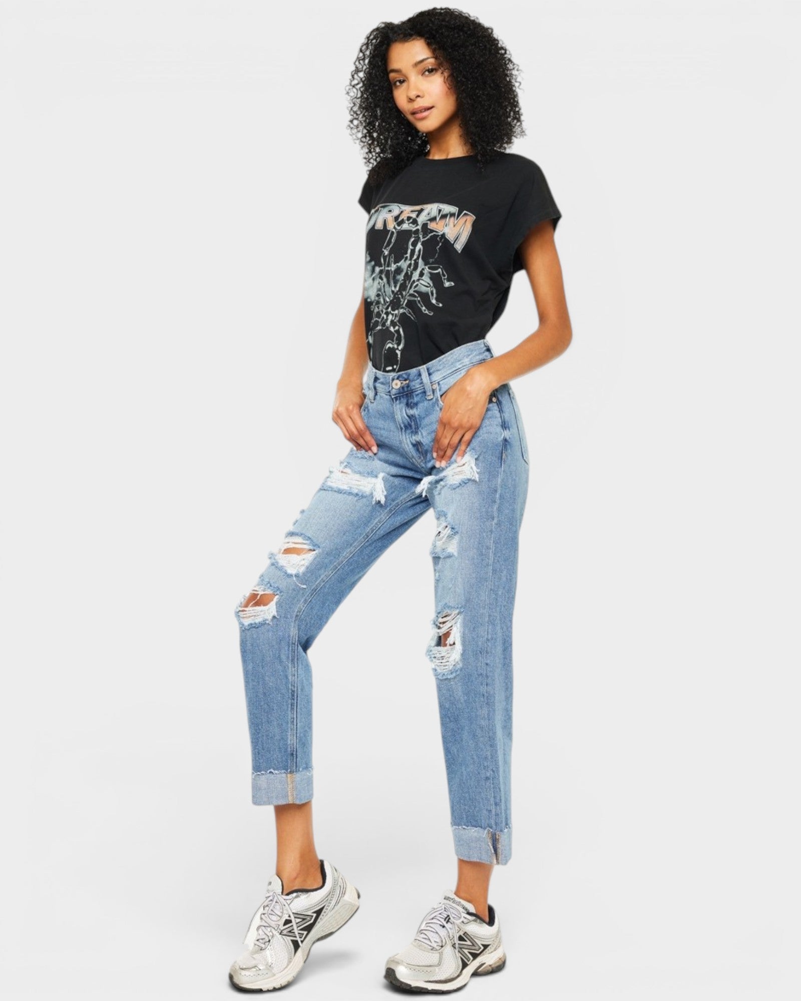 Woman wearing a black graphic t-shirt and light blue ripped jeans on a white background