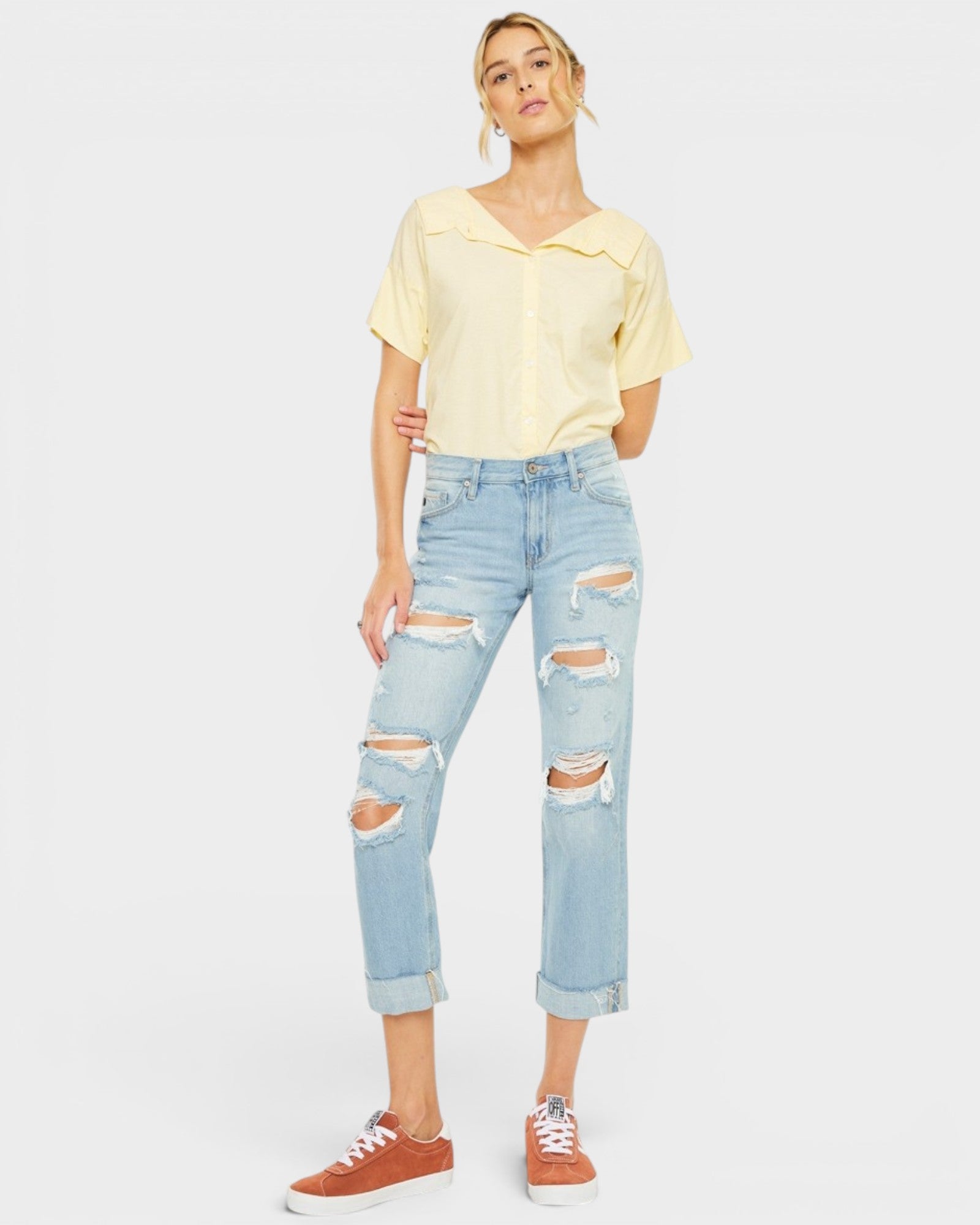 Woman wearing a yellow top and light blue ripped jeans on a white background