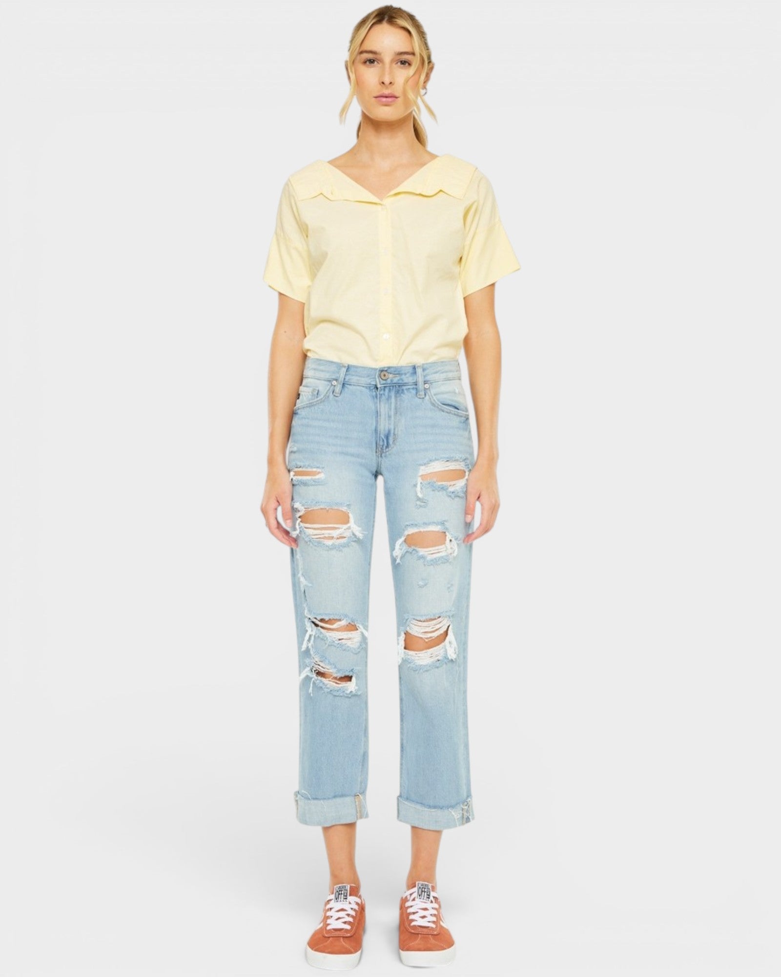 Person wearing a yellow top and light blue ripped jeans on a white background