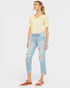 Woman wearing a yellow top and light blue ripped jeans on a white background