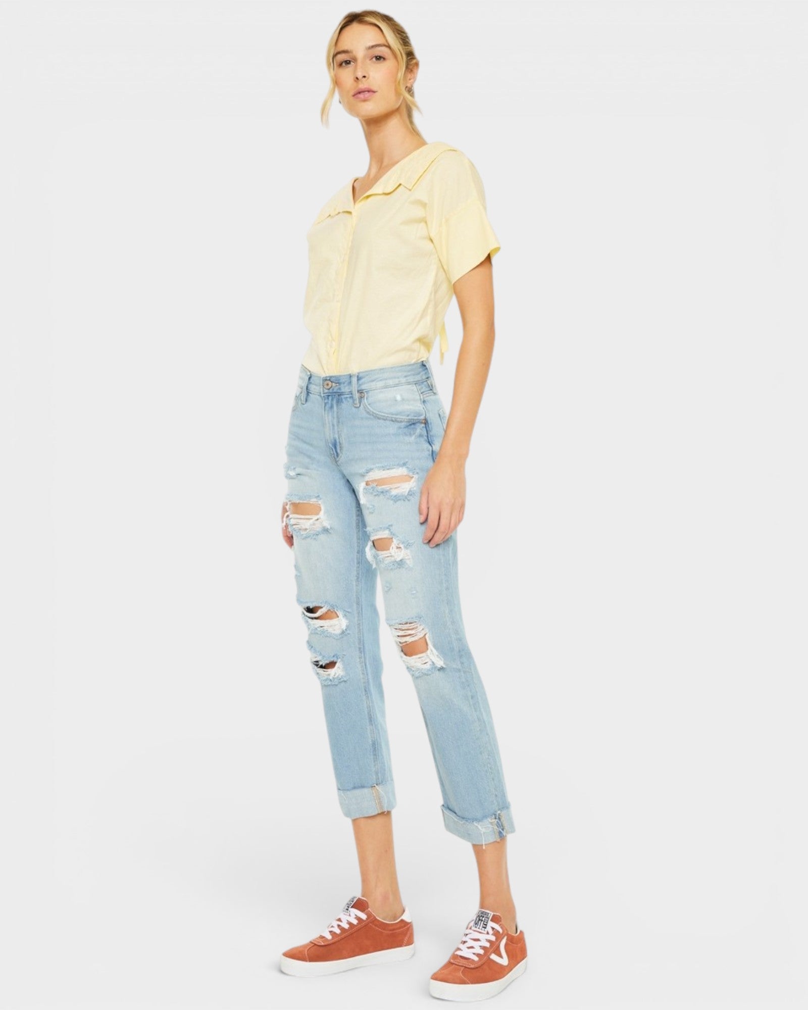 Person wearing a yellow shirt and light blue ripped jeans on a white background