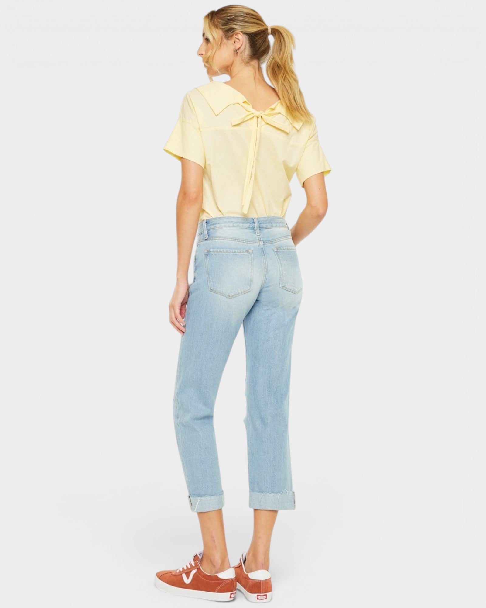 Woman wearing a yellow top and light blue jeans on a white background