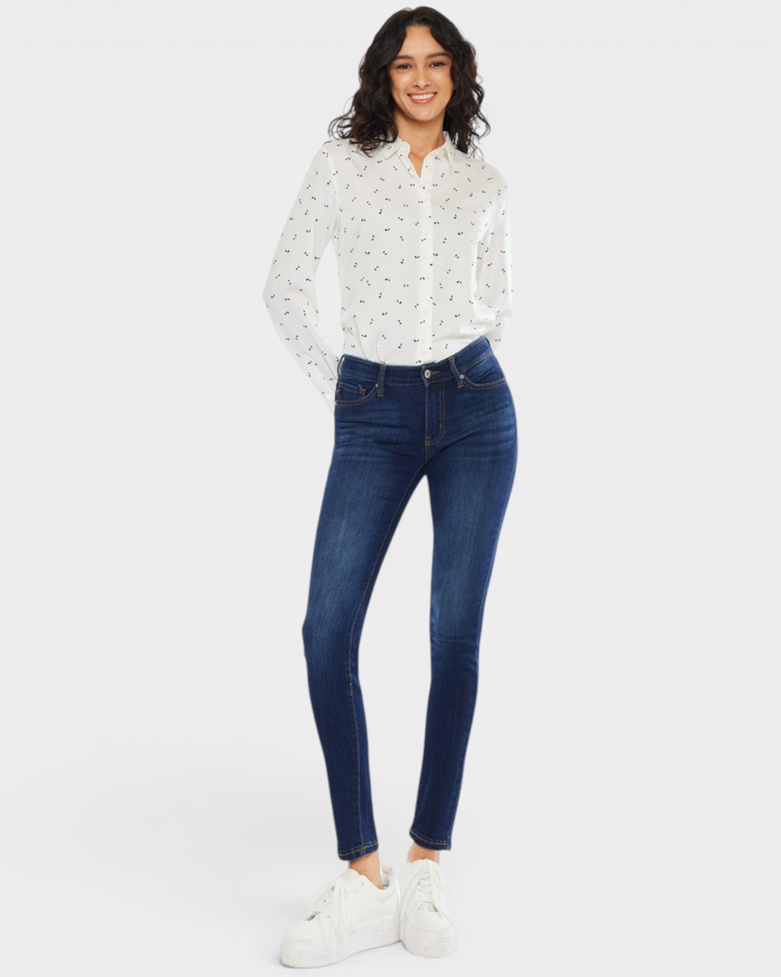 Woman wearing a white polka dot shirt and blue jeans on a white background