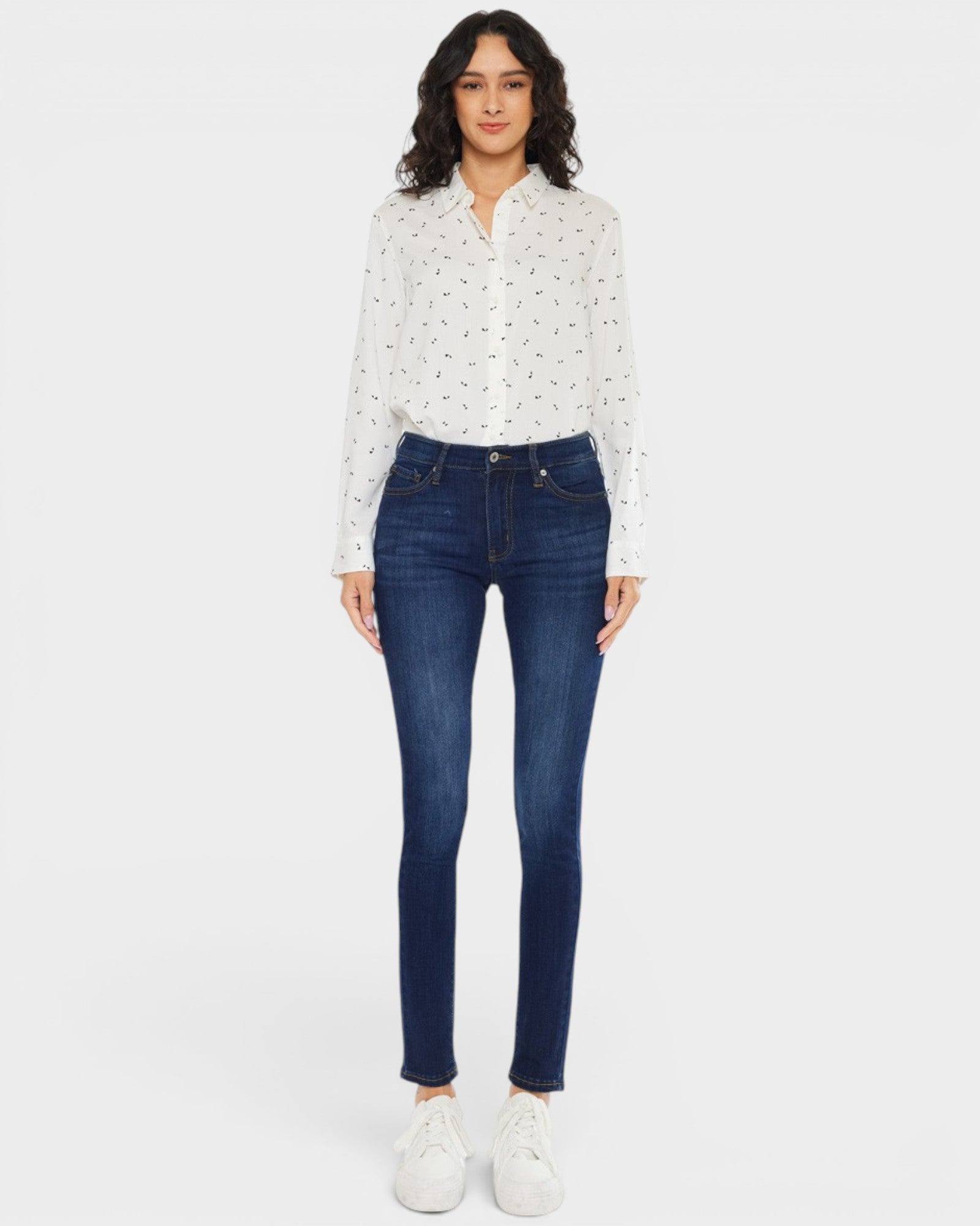 Woman wearing a white blouse with black patterns and blue jeans on a white background