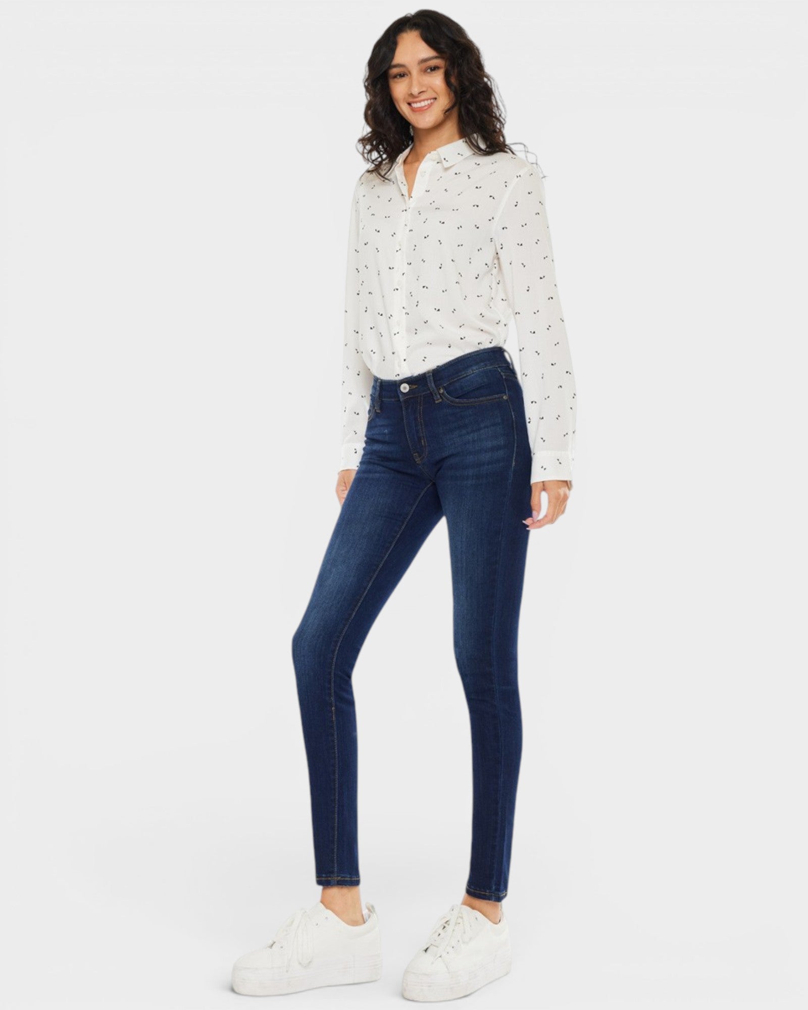 Woman wearing a white blouse with black patterns and dark blue jeans on a white background