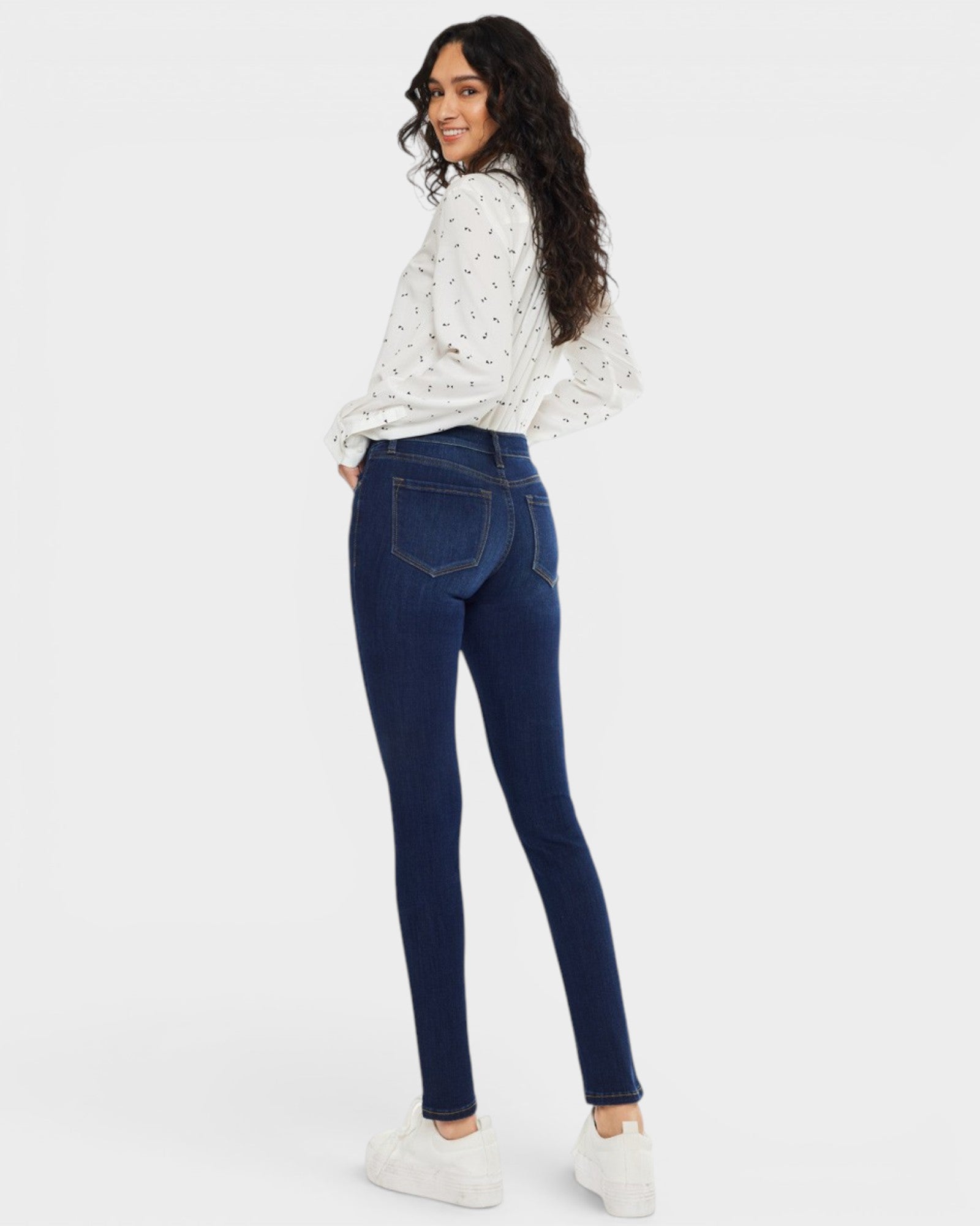 Woman wearing blue jeans and a white patterned top on a white background