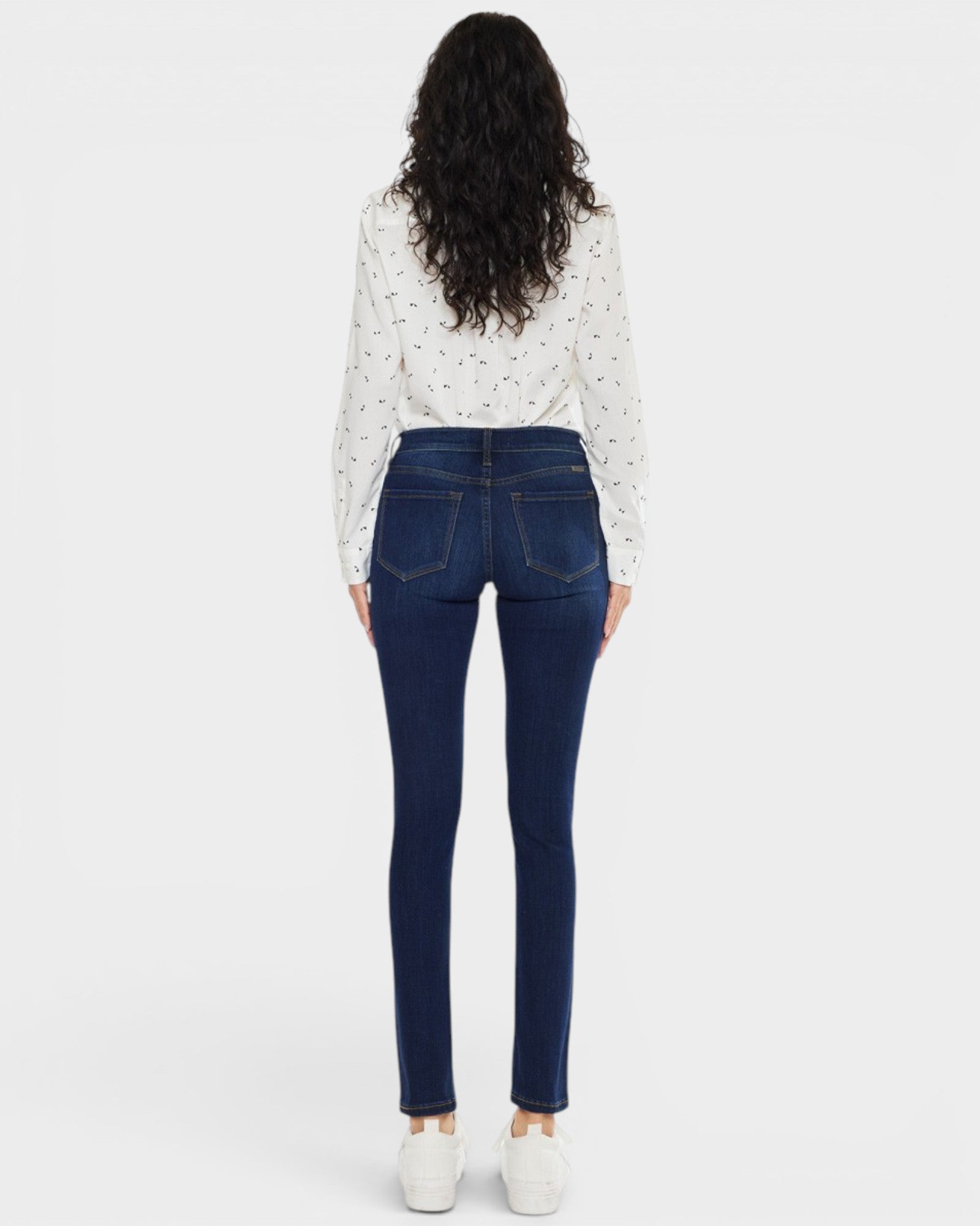 Woman wearing blue jeans and a white blouse with black patterns on a white background