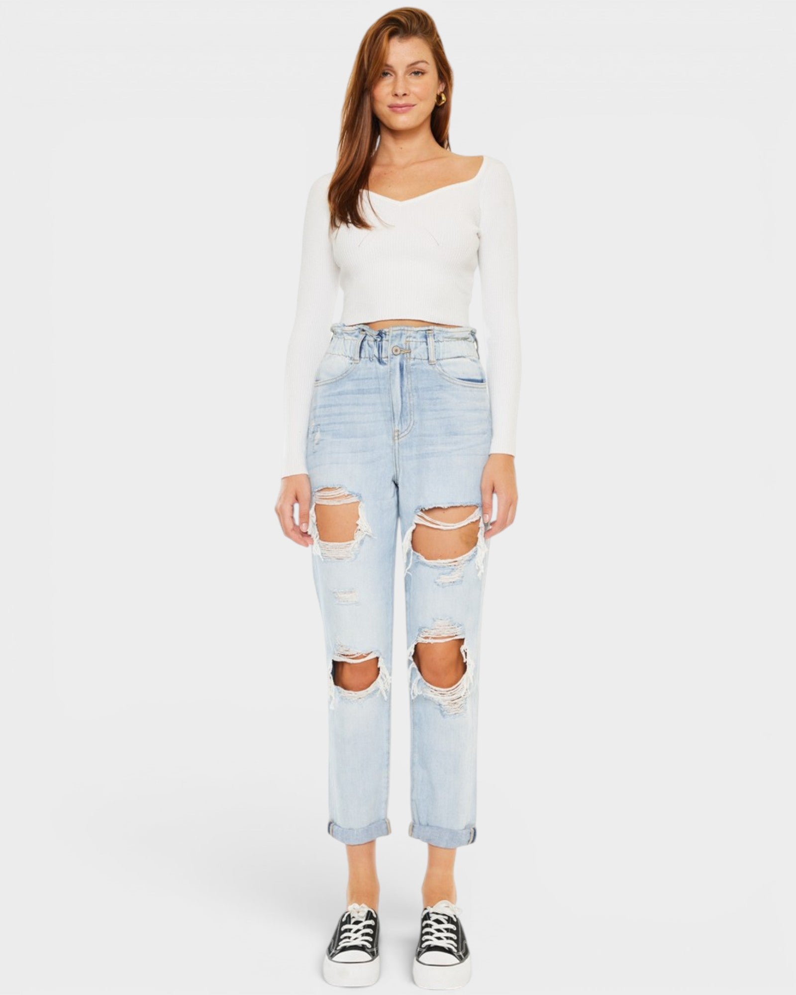 Woman wearing a white long-sleeve top and light blue ripped jeans on a white background