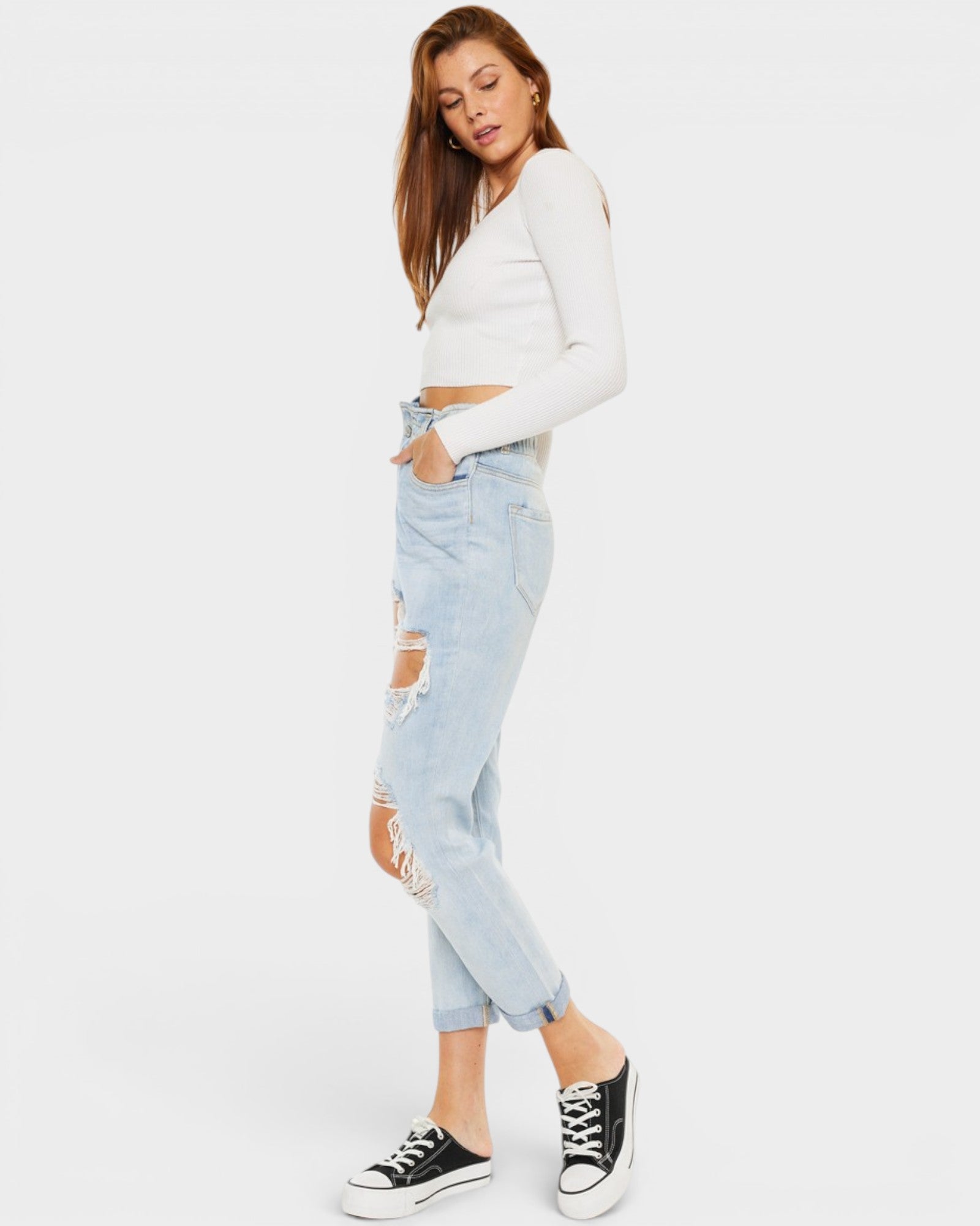 Woman wearing a white long-sleeve top and light blue ripped jeans on a white background