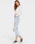 Woman wearing a white long-sleeve top and light blue ripped jeans on a white background