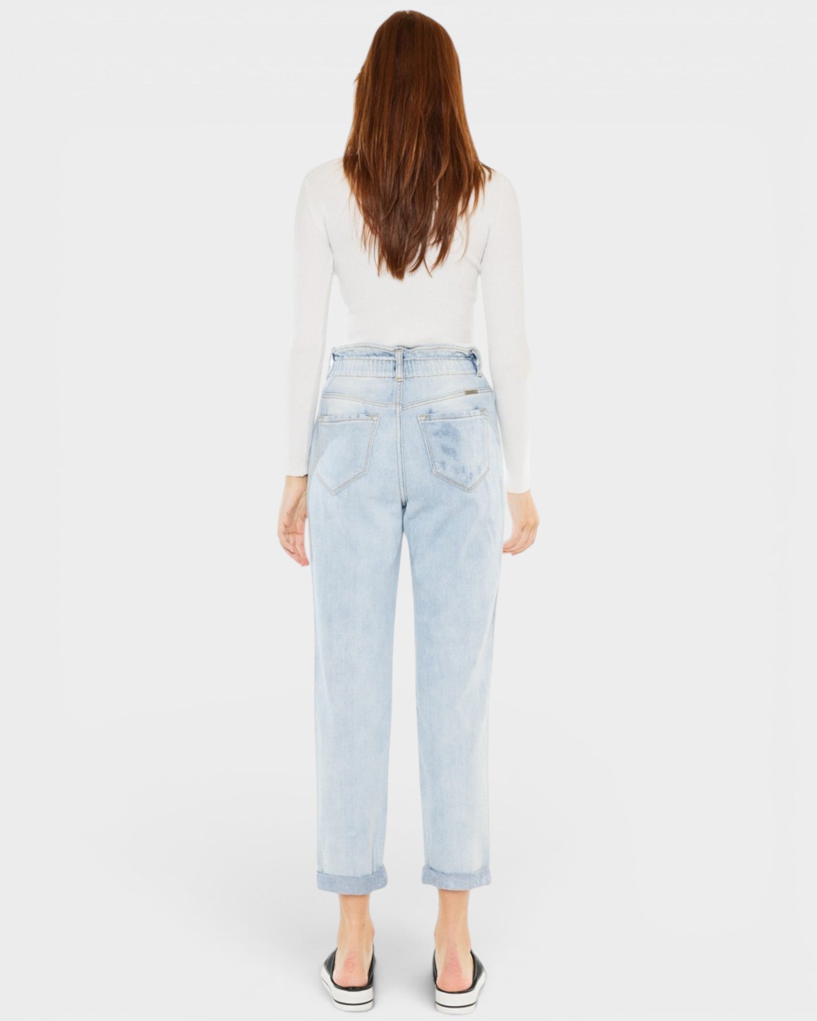 Person wearing light blue jeans and a white top on a plain background