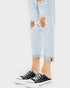 Person wearing black sneakers with white laces and light blue ripped jeans on a white background
