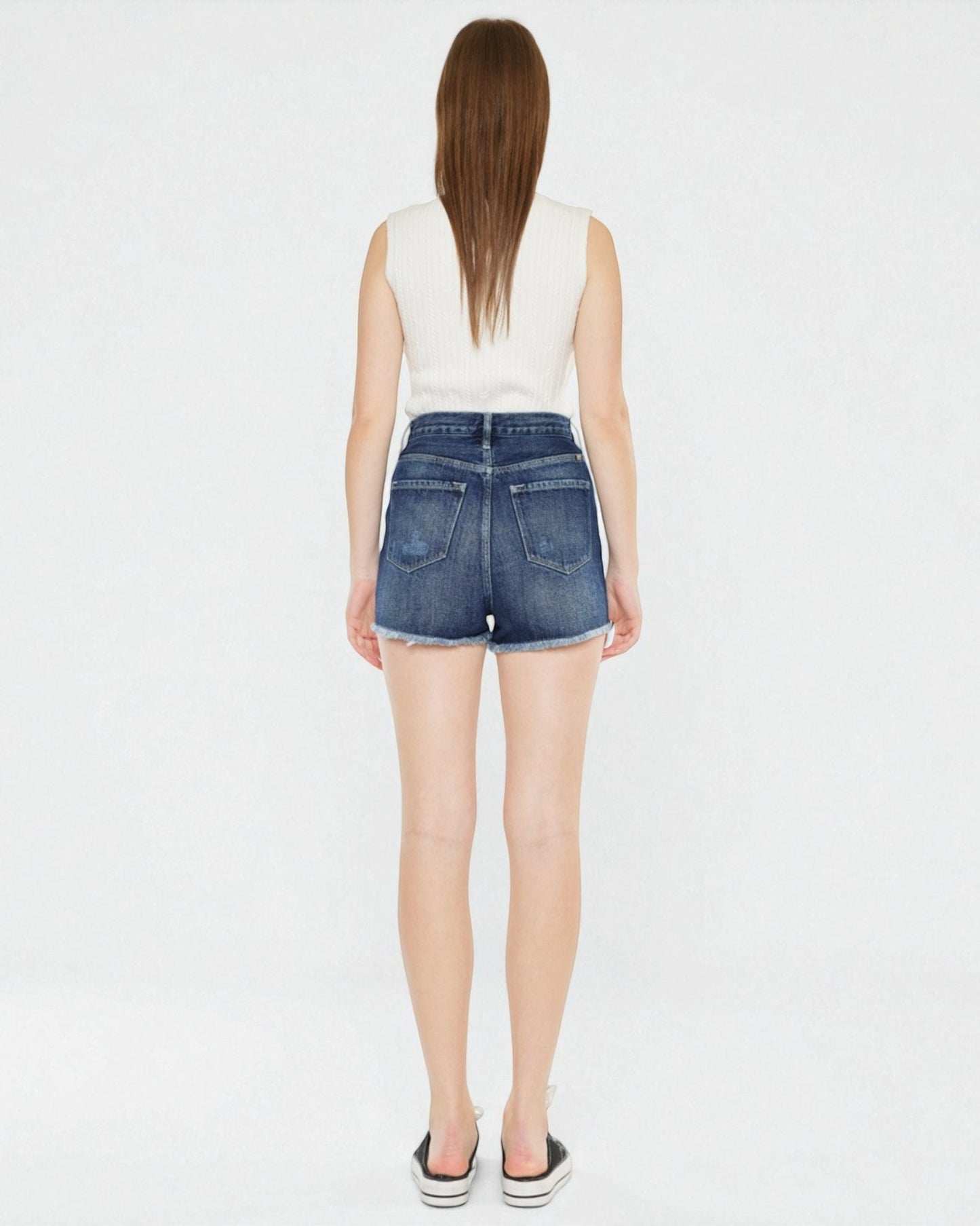 Person wearing a white sleeveless top and blue denim shorts on a white background
