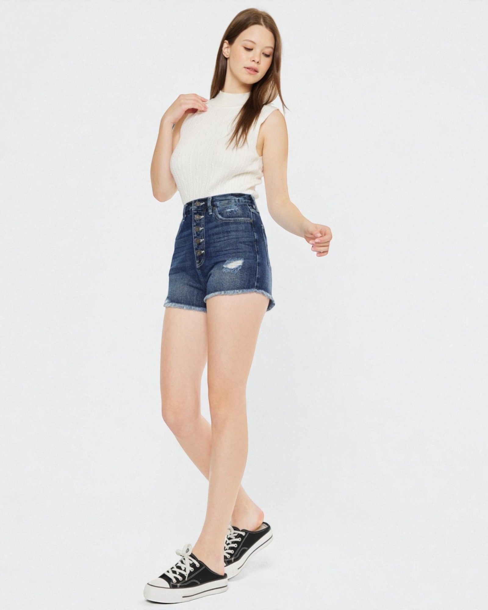 Woman wearing a white sleeveless top and blue denim shorts on a white background