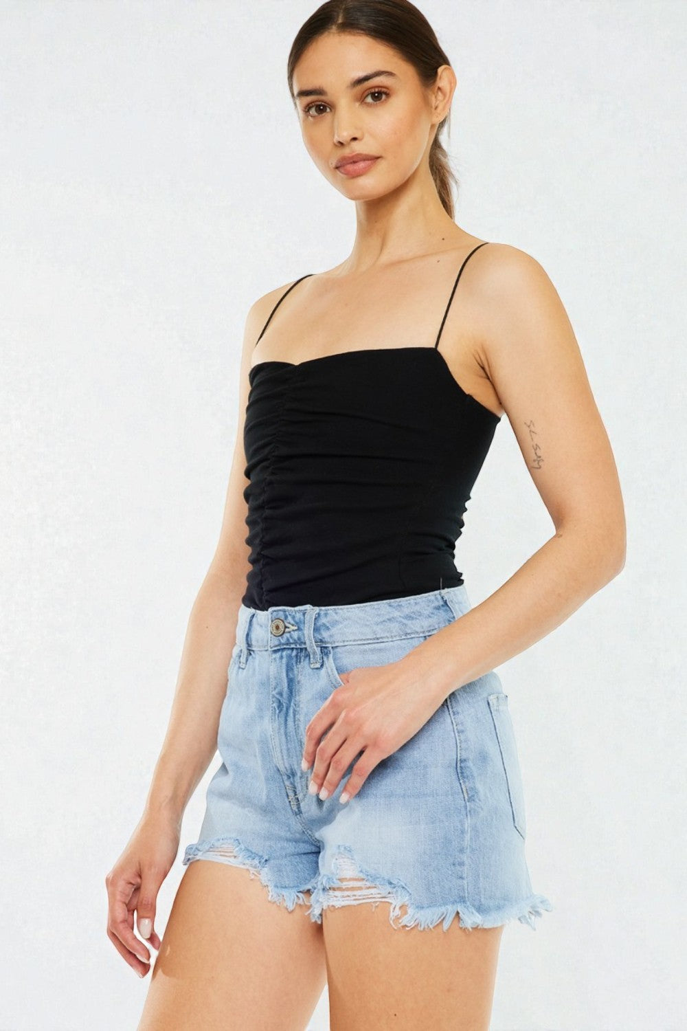 Woman wearing a black strap top and light blue denim shorts on a white background