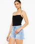 A woman modeling a black ruched spaghetti-strap camisole top paired with light-wash distressed denim shorts against a plain white studio background.