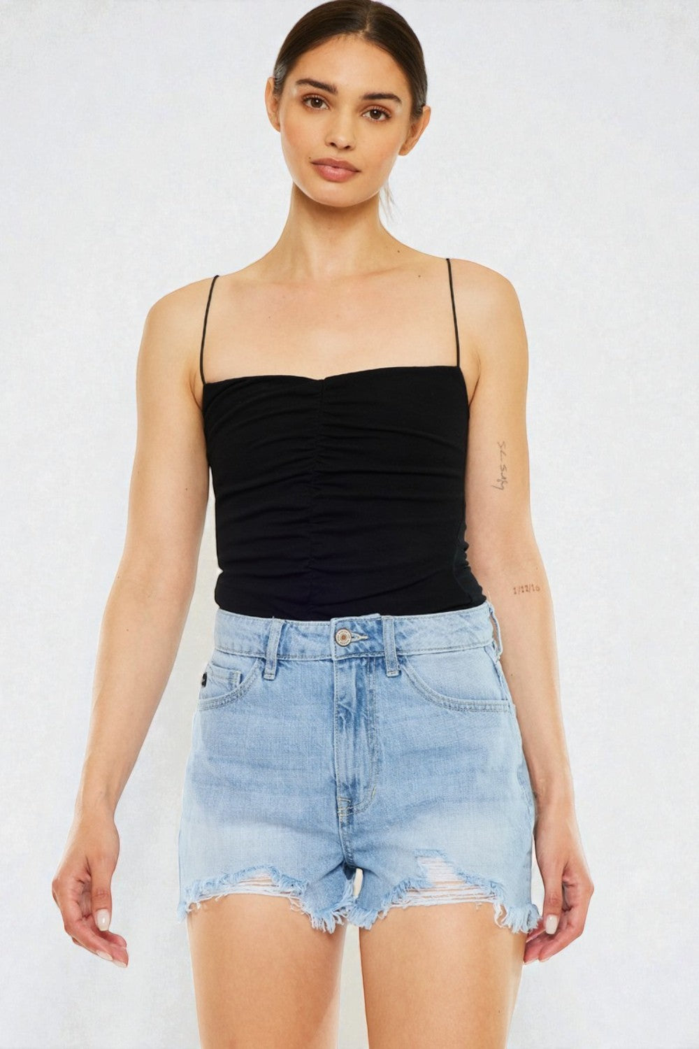 Woman wearing a black strap top and light blue denim shorts on a white background