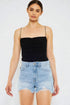 Woman wearing a black strap top and light blue denim shorts on a white background