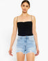 A woman modeling a black ruched spaghetti-strap camisole top paired with light-wash distressed denim shorts against a plain white studio background.