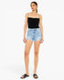 A woman modeling a black ribbed camisole top and light-wash denim shorts against a plain white studio background.
