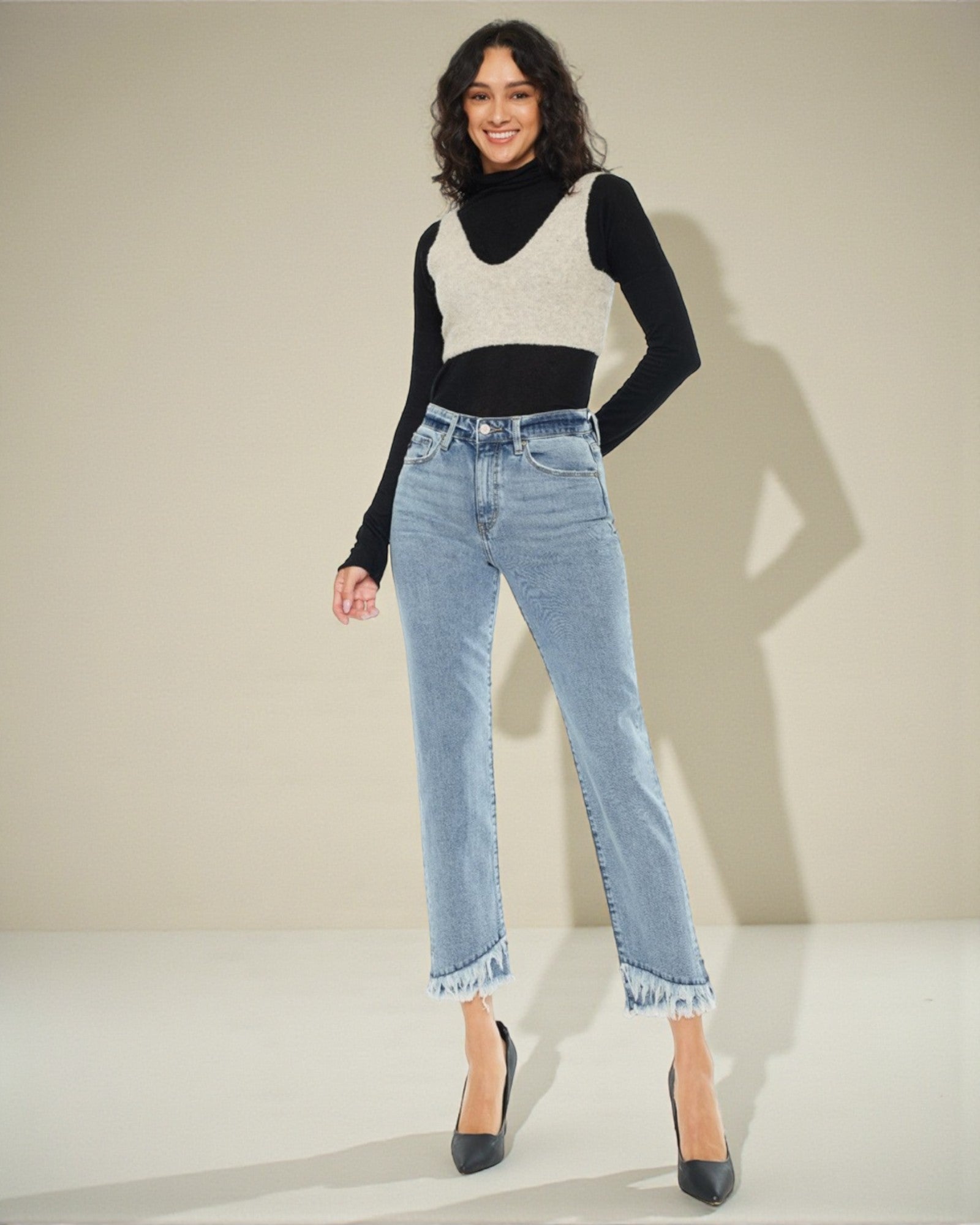 Woman wearing a black and white top with a black turtleneck and light blue jeans on a beige background