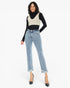 A model wearing a black long-sleeve turtleneck sweater layered under a cream knit vest, paired with light-wash frayed hem jeans and black pointed-toe heels, against a plain white studio background.