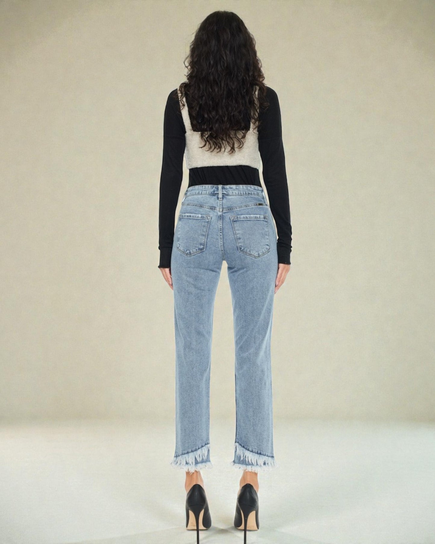 Woman wearing light blue jeans and a black long-sleeve top on a plain background