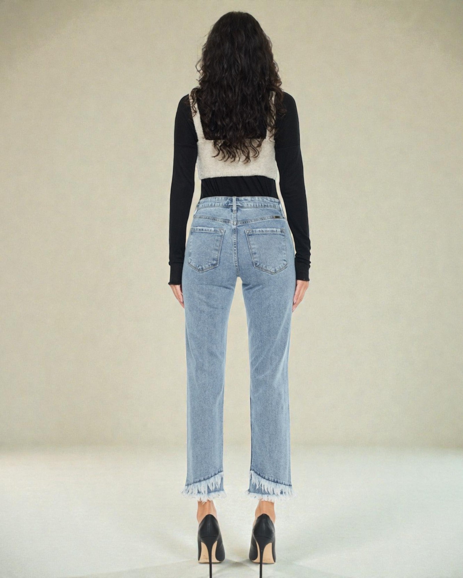 Woman wearing light blue jeans and a black long-sleeve top on a plain background