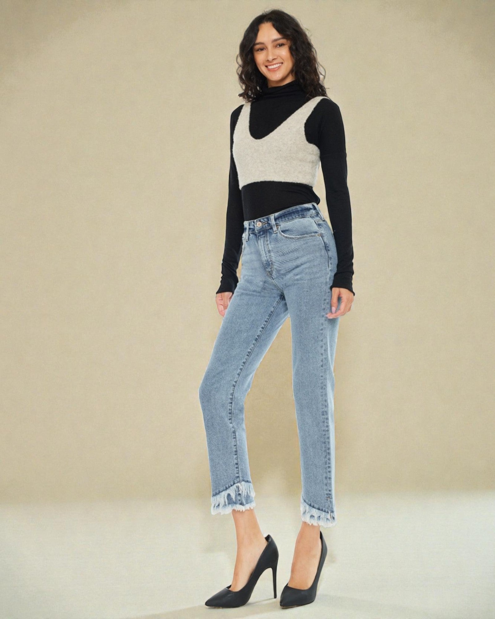 Woman wearing a black and white top with blue jeans on a beige background