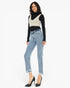 A woman modeling a pair of light-wash blue cropped jeans with frayed hems, styled with a black long-sleeve top, a beige knit vest, and black high heels against a plain white background.