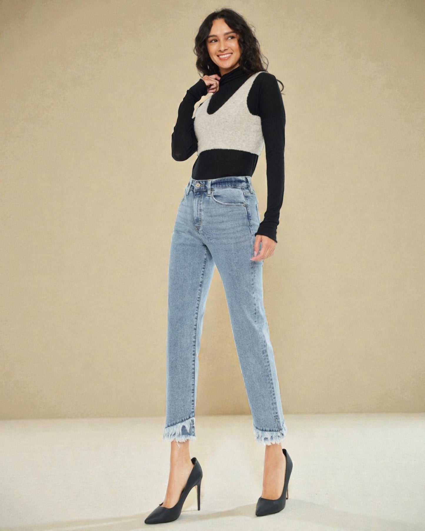 Woman wearing a black long-sleeve top, white sleeveless vest, and light blue jeans against a beige background