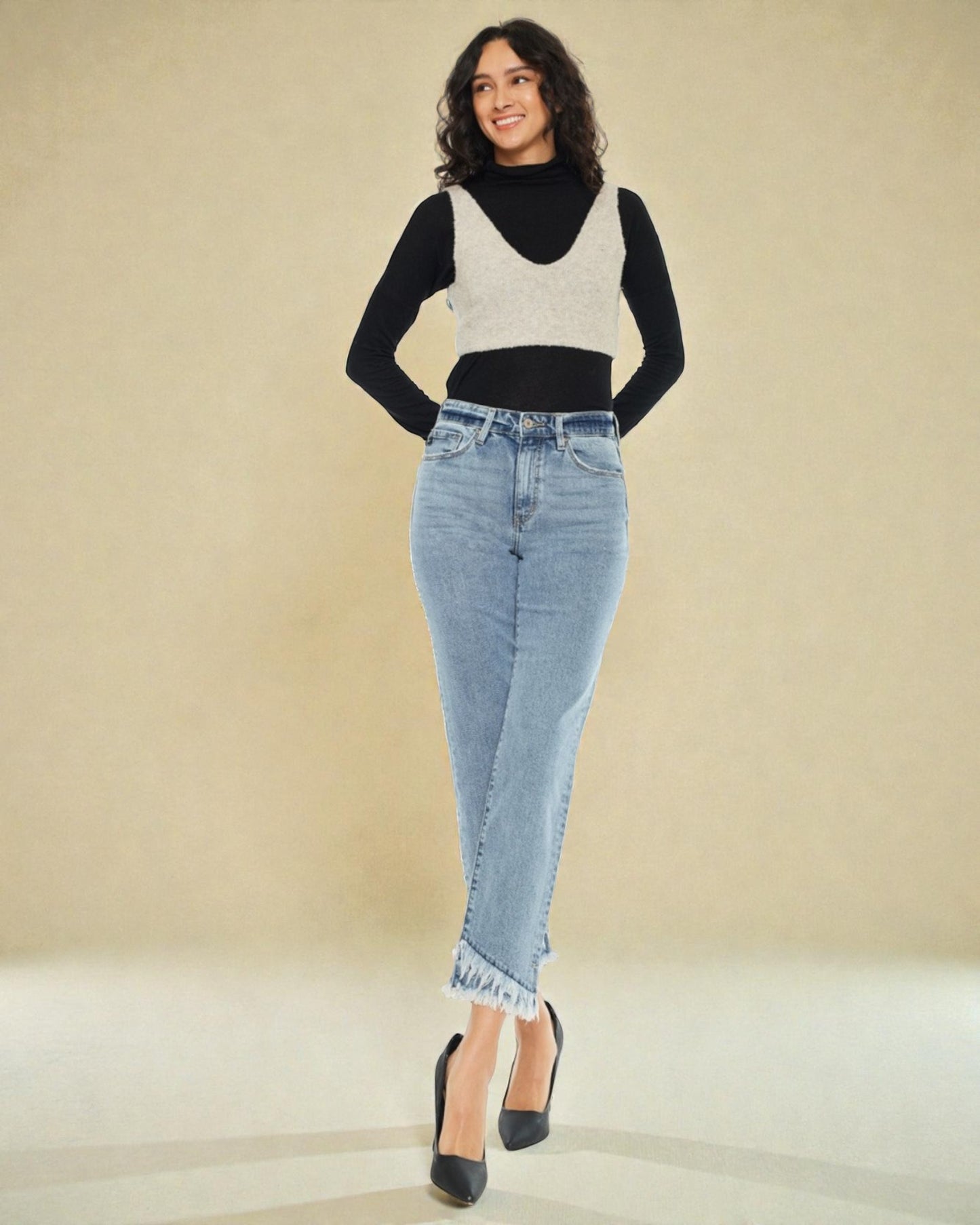 Woman wearing a black and white sweater with a black top and blue jeans on a beige background