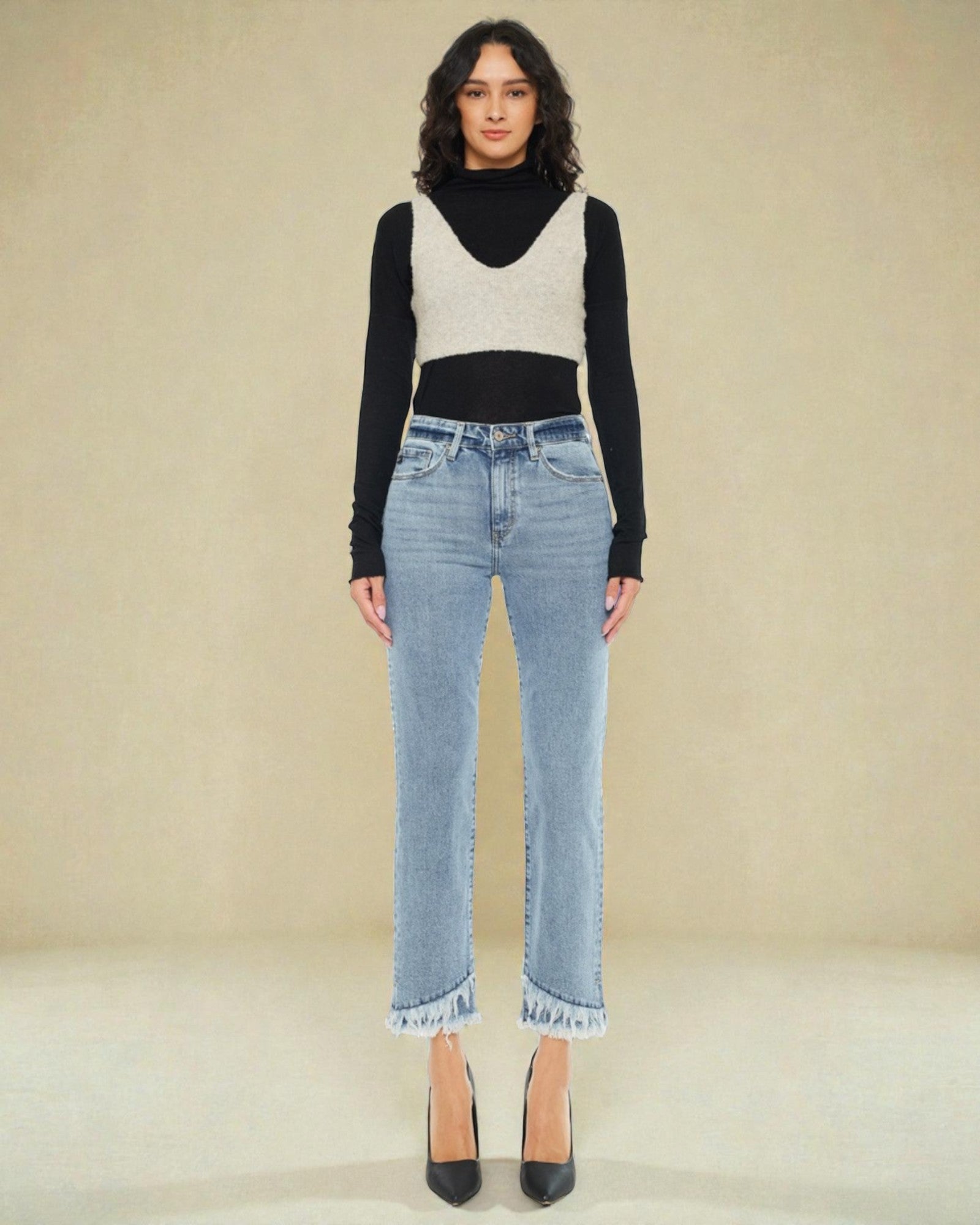 Woman wearing a black long-sleeve top, white sweater, and light blue jeans on a beige background