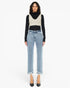 A model stands against a plain white studio background wearing a black long-sleeve turtleneck, a cream knit vest, light-wash blue cropped jeans with frayed hems, and black pointed heels.