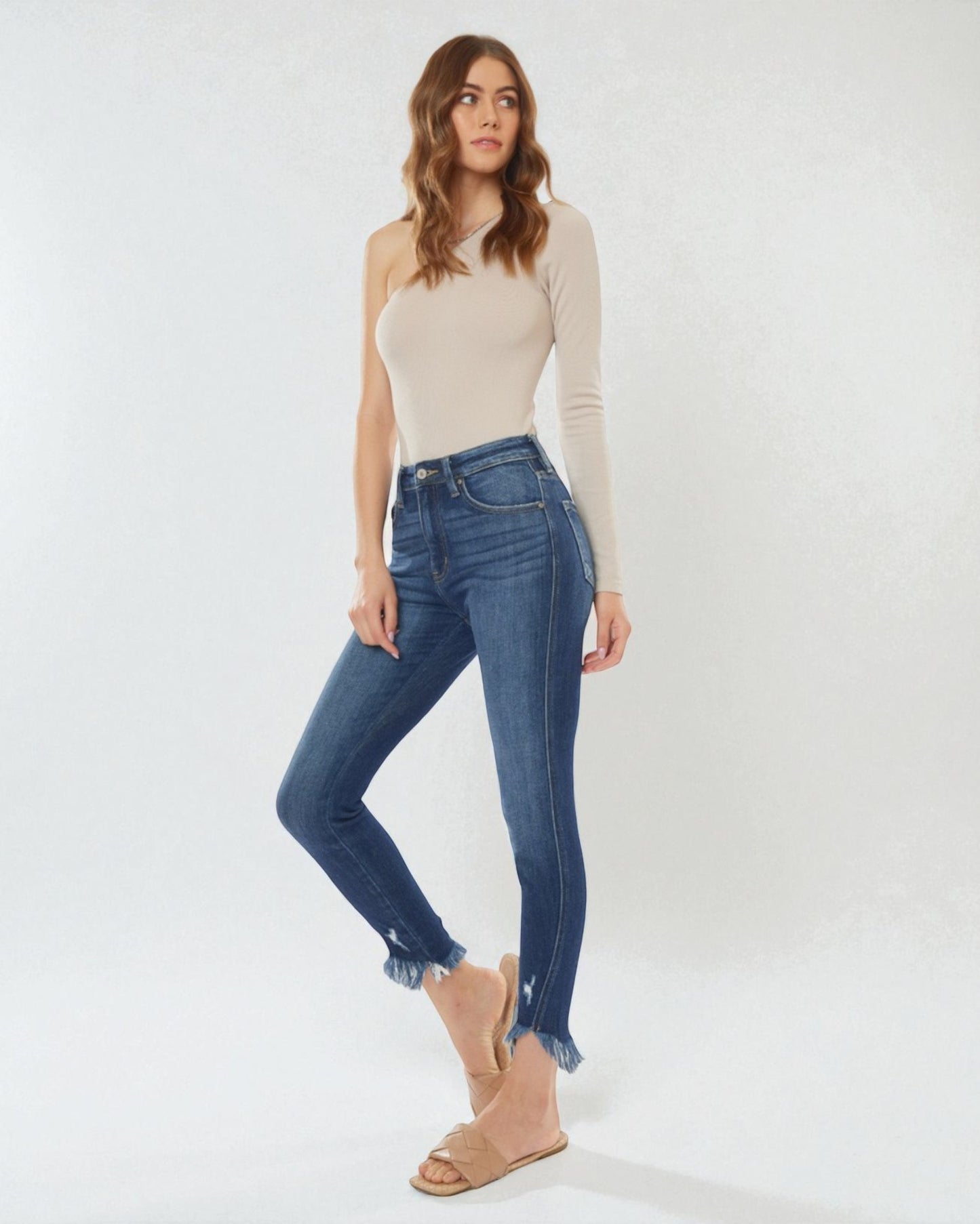 Woman wearing a beige long-sleeve top and blue jeans on a white background