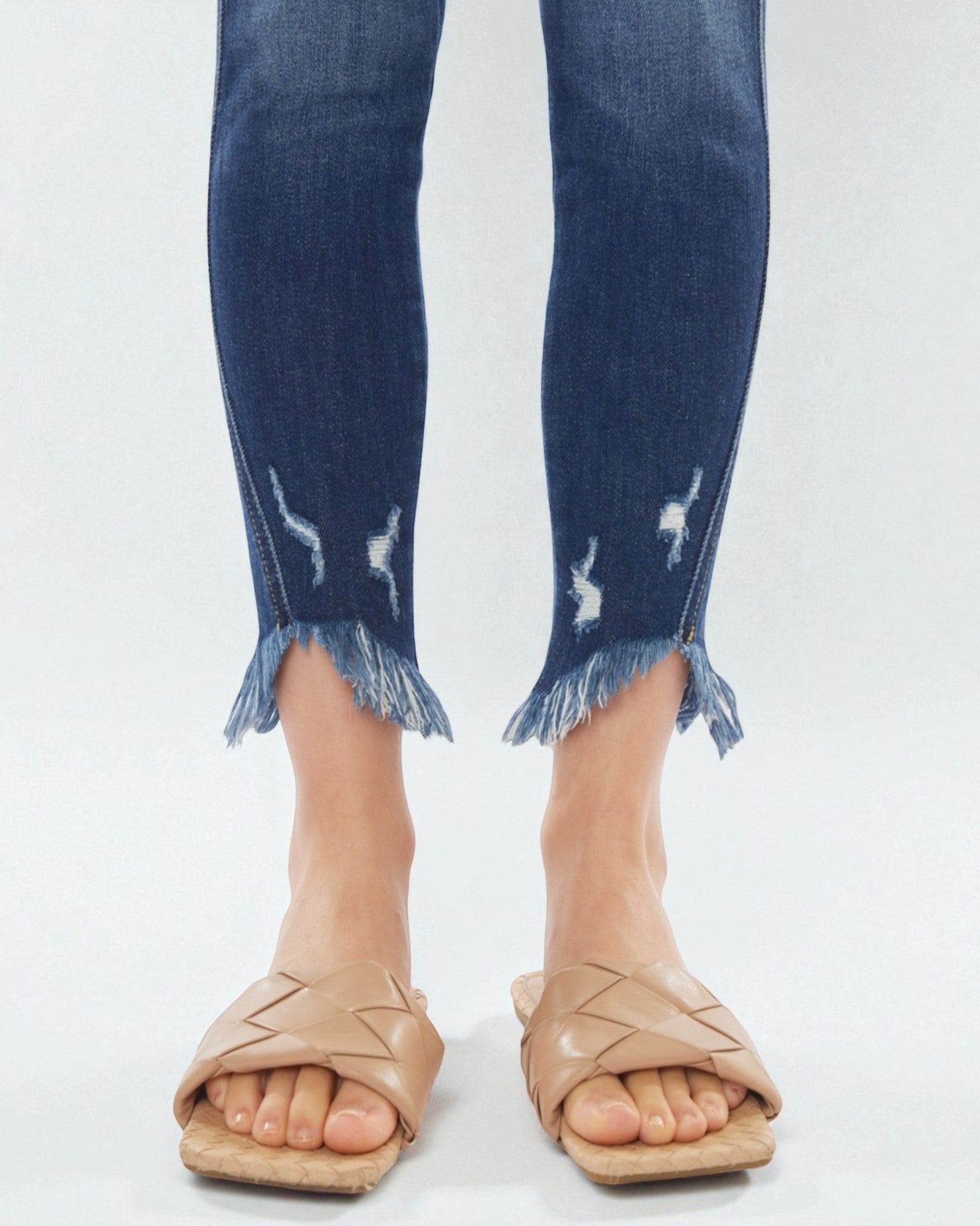 Person wearing blue jeans with fringe hem and beige sandals on a white background